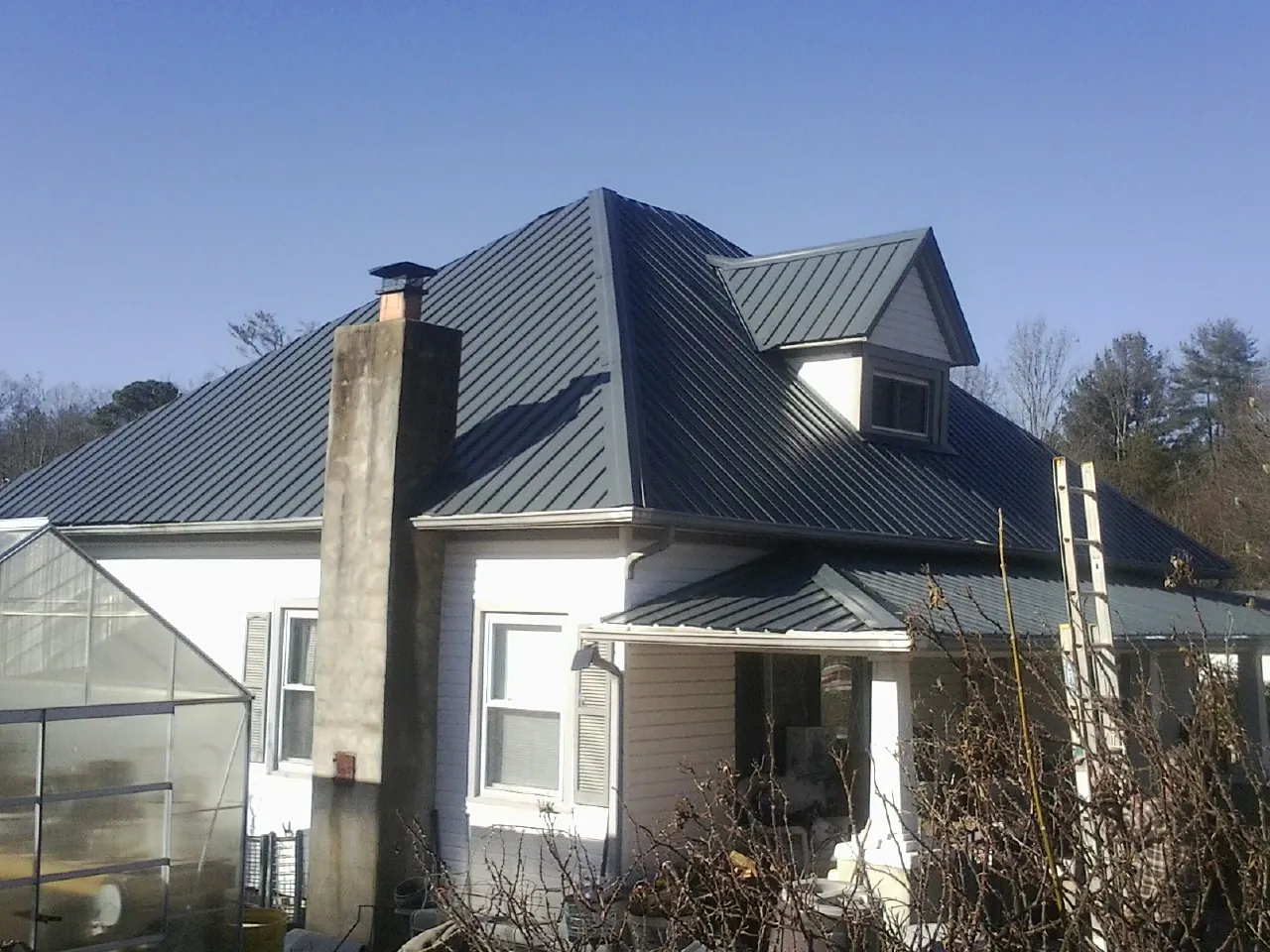 Dark blue standing seam metal roof on a white farmhouse with dormer — Slate & Tile Roof Repair by Roofing Brothers in Seanor