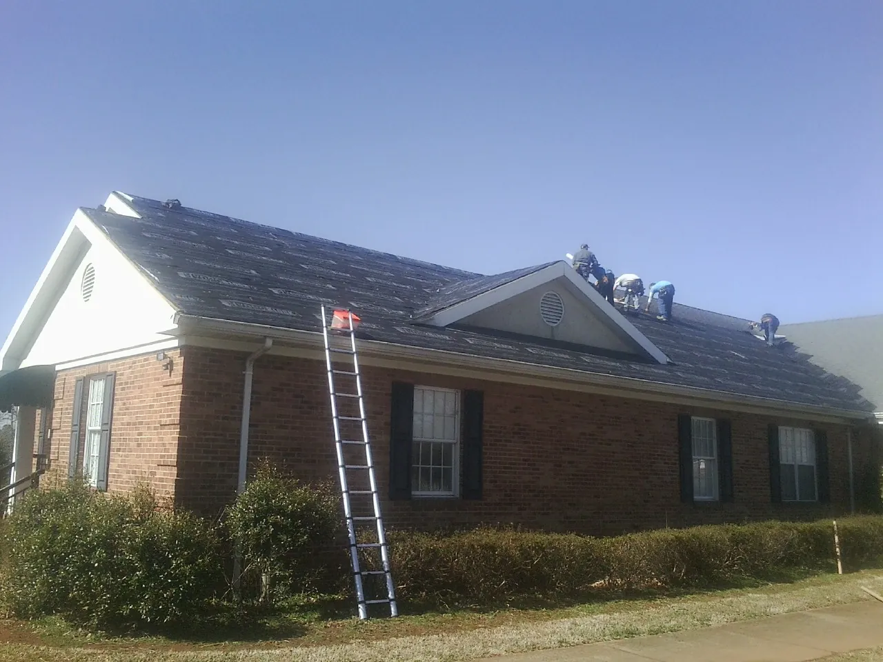 Crew tearing shingles off a brick ranch roof with a ladder set — Metal Roof Repair work by our crew in Seanor