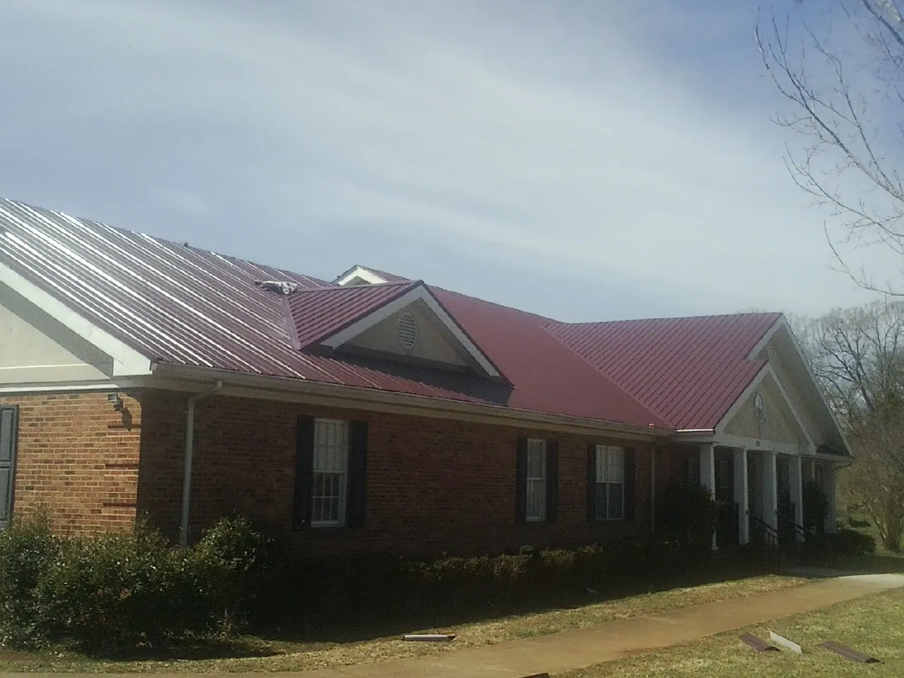 Red metal roof with gabled entries on a long brick building, from a Hail Damage Roof Repair job in Seanor