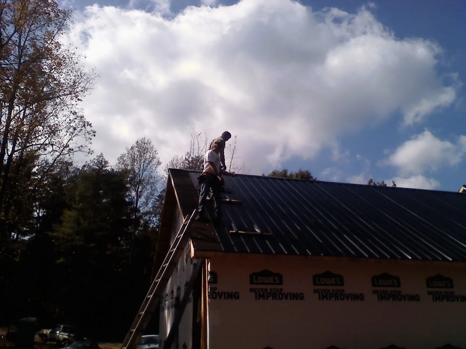 Roofer fastening dark metal panels high against a cloudy sky, from a Roof Inspection job in Seanor
